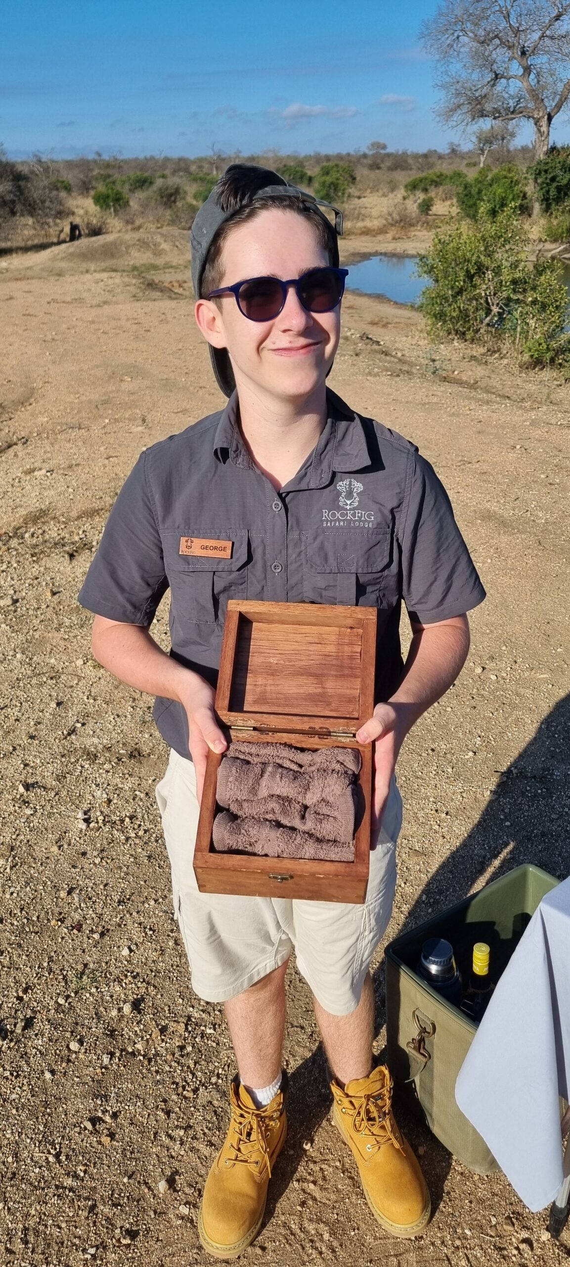George in his Rockfig uniform and name badge at a bush stop by a waterhole